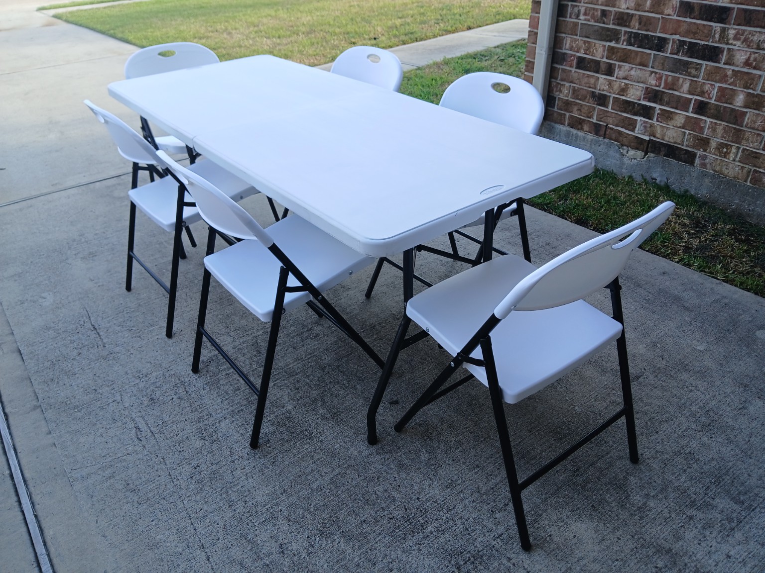White folding table with six white chairs available to rent